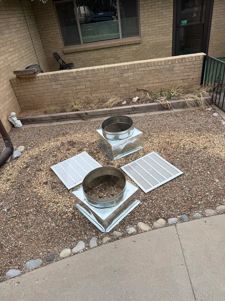 Duct boots and register grilles staged on gravel before install