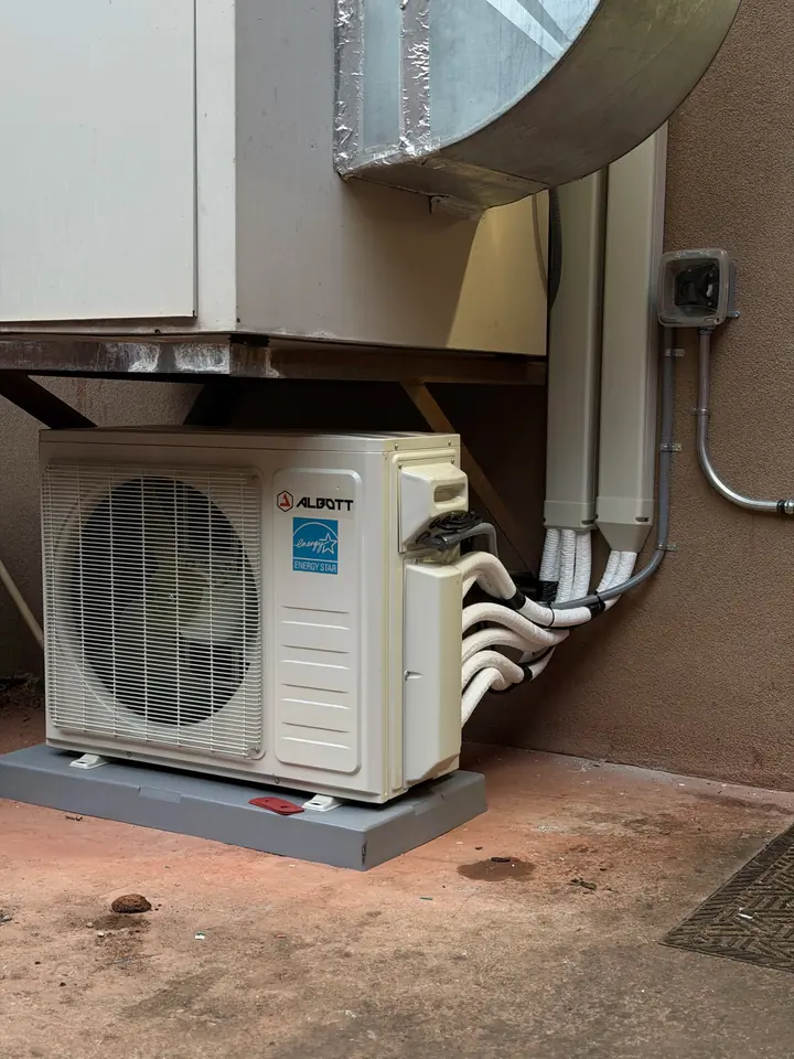 Mini split outdoor unit on a rooftop stand beside ductwork