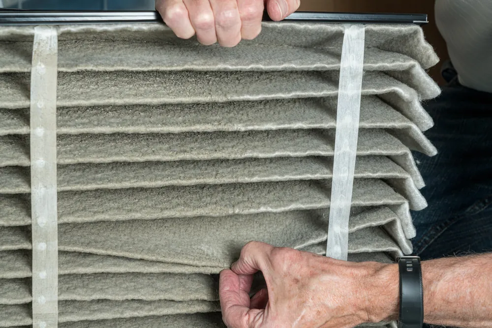 Hands pulling a pleated air filter out of its slot for inspection
